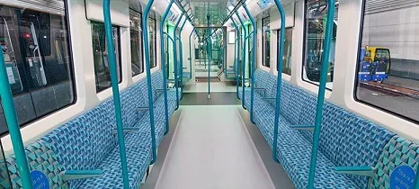 Interior of new DLR train showing open gangways, light blue moquette, & transverse seating