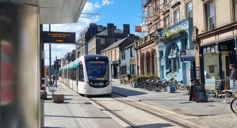 Edinburgh tram approaching a stop on the just opened Newhaven extension, with old shops in background
