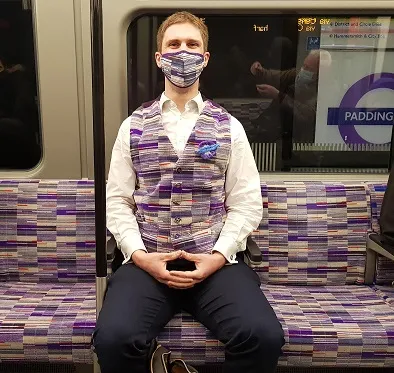 Man in self-made Elizabeth line purple moquette vest & mask on Eliz line train