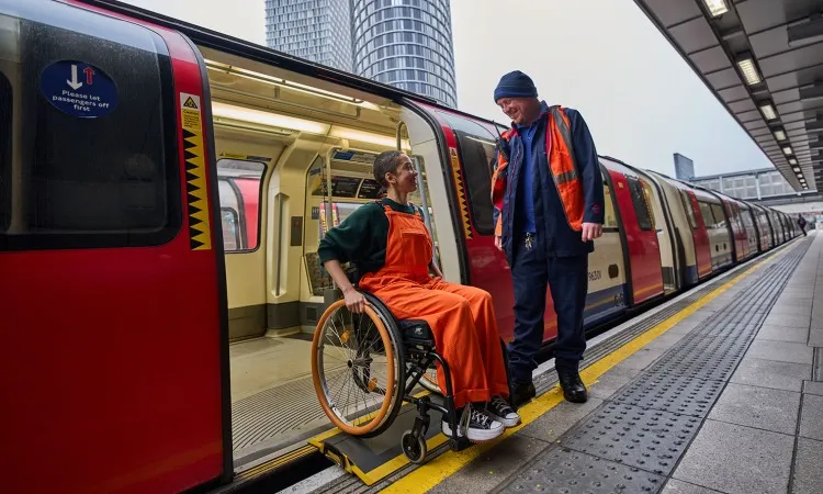 Photo of Tube train gap bridging ramp in used on an open Tube train down, by a person in a wheelchair, watched by a TfL staff