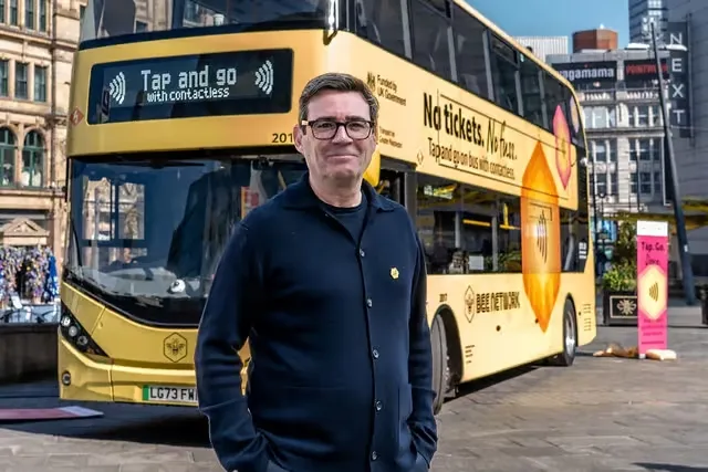 Manchester Mayor Andy Burnham in front of yellow Bee Network bus. TfGM